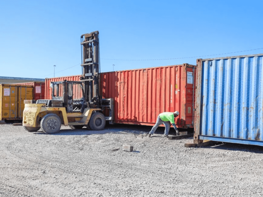 A lift lifting a shipping container on a yard.