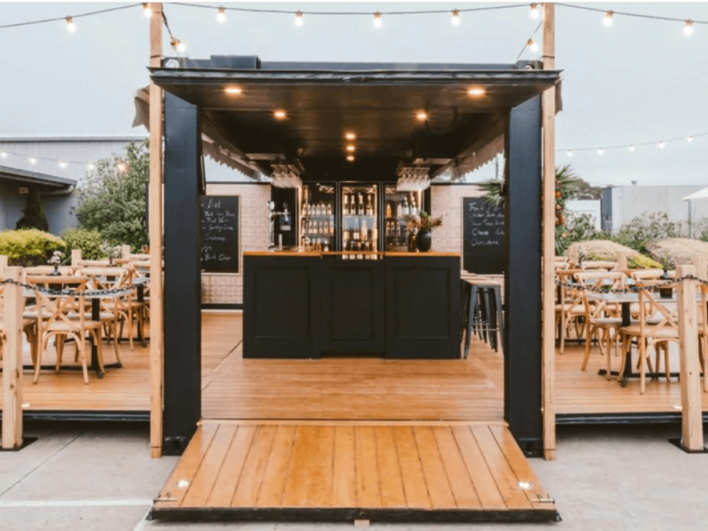 Open concept shipping container bar featuring seating and string lights.