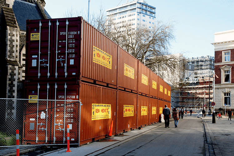 A group of shipping containers stacked along a street in a city as part of a construction project.