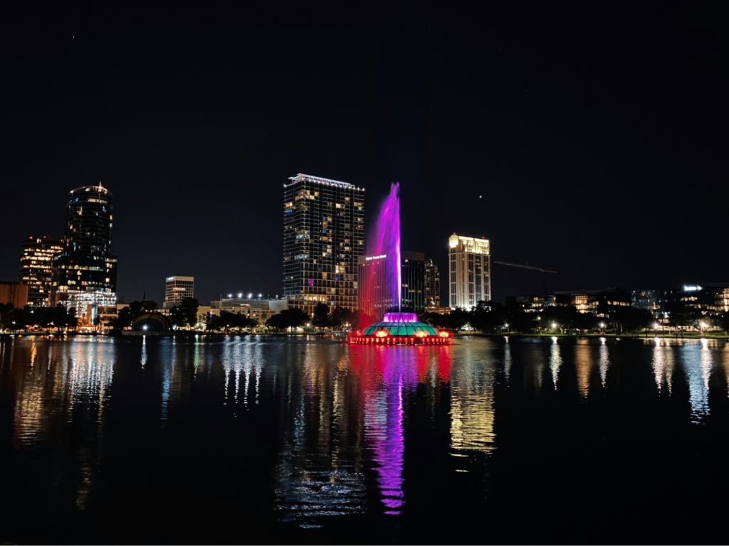 A fountain lit up at night with downtown Orlando in the background.