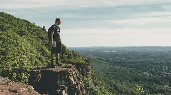 A man standing on edge of a forest cliff.