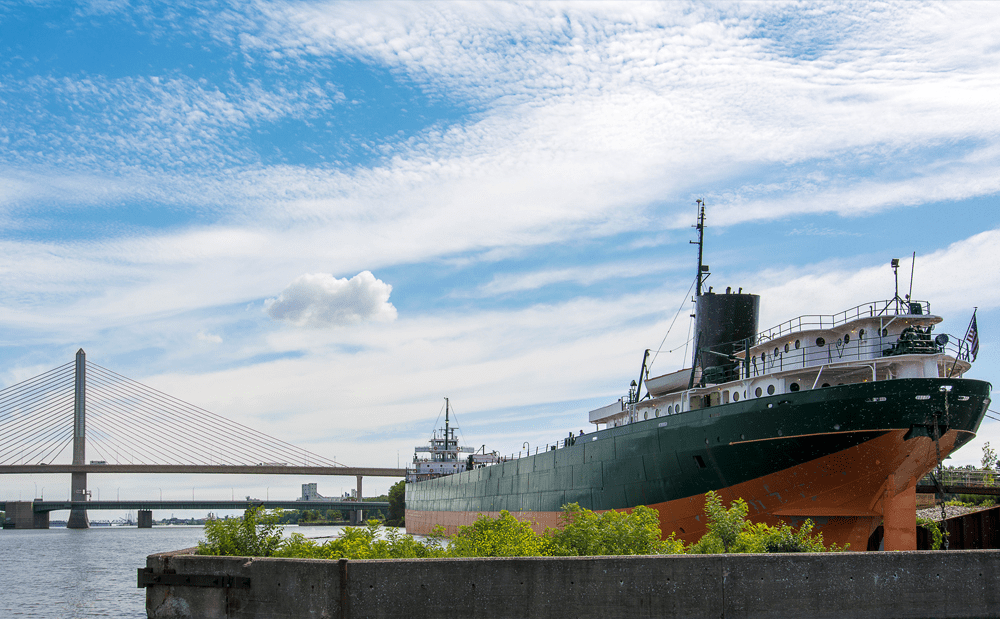 A large ship on Lake Erie with a bridge in the background.