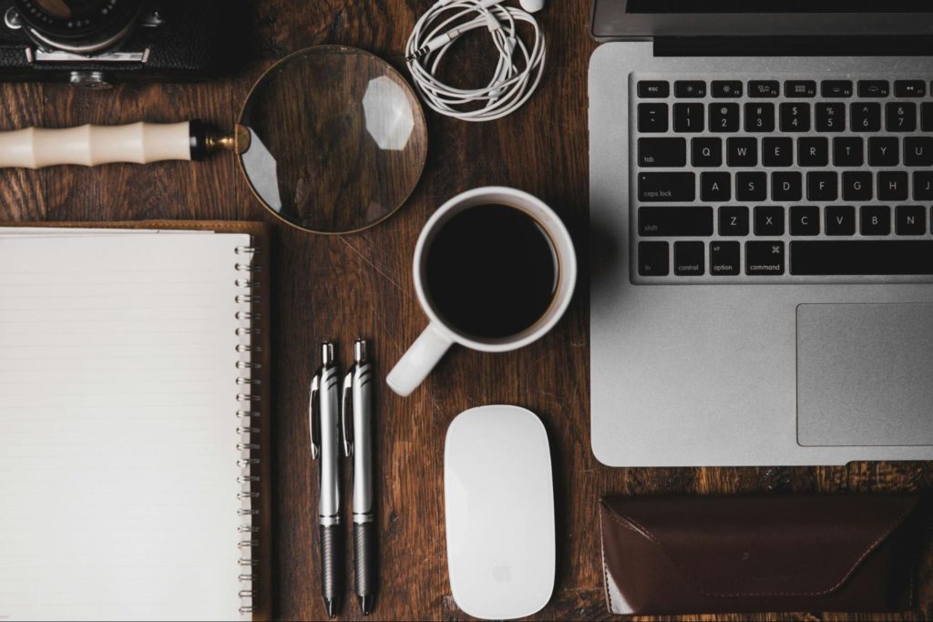 A close up look at someone's office setup with laptop, mouse, coffee cup, pens & more